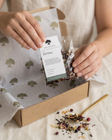 Hands lifting a loose leaf tea sample pouch from the tea sampler box